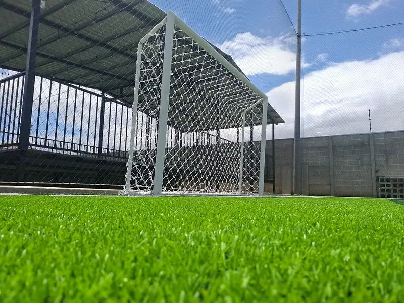 Marco de fútbol con red blanca en cancha sintética, con la malla perimetral al fondo