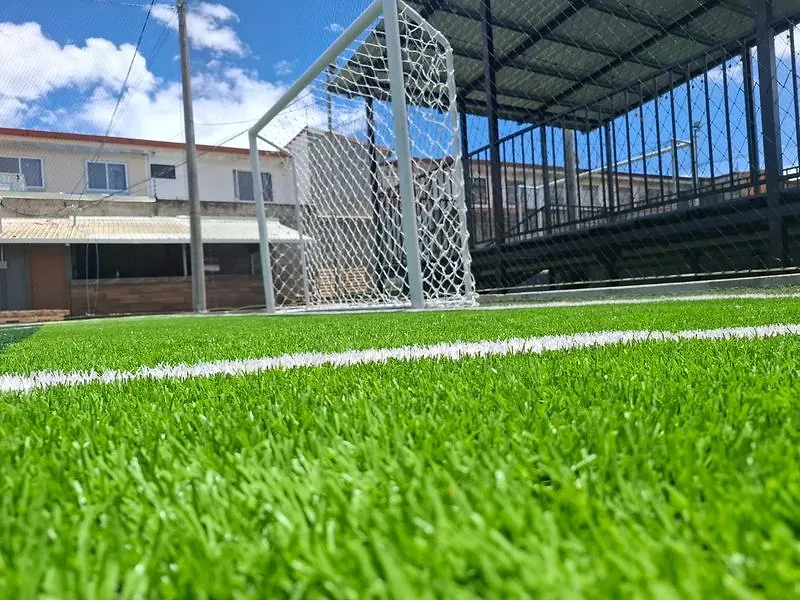 Portería con red blanca en cancha de césped sintético, vista a ras de grama